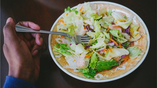 A hand holding a fork in a salad dish