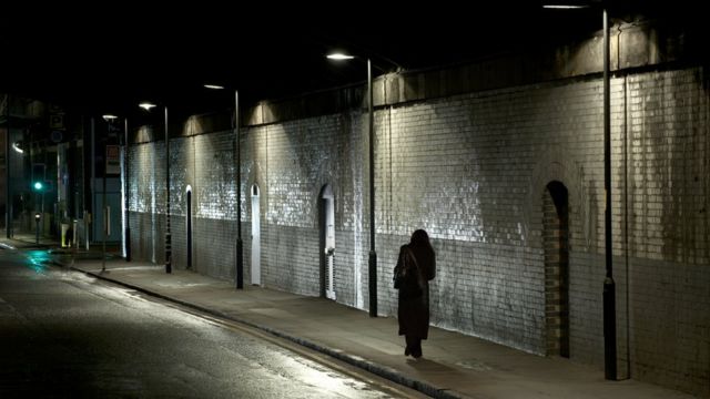A woman walks alone along a street at night