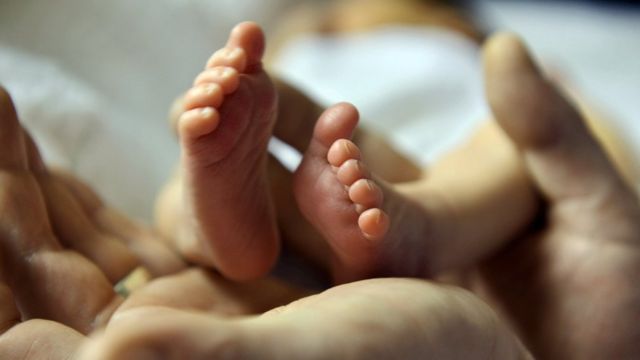 A father cradles the tiny feet of his five-day-old baby girl