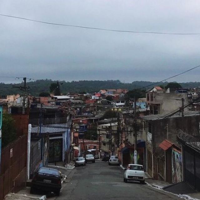 Imagem mostra uma rua de Vila Flavia, comunidade do distrito de São Mateus, com carros estacionados e céu nublado