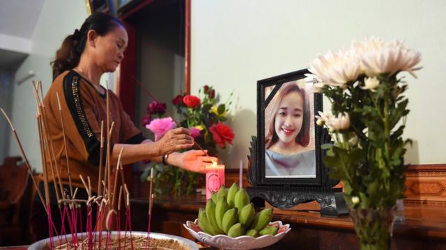 A relative lights an incense stick in front of a portrait of Bui Thi Nhung
