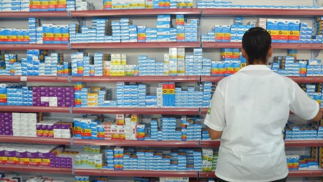 Farmacêutica de costas em frente a prateleiras de medicamentos
