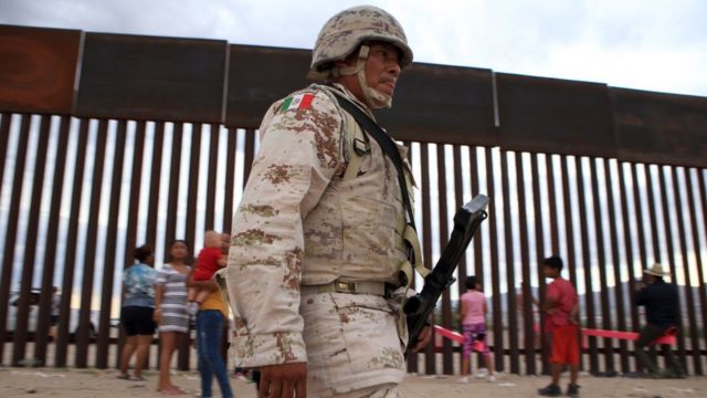A Mexican soldier walks past children playing at the border