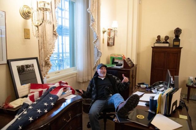 这名抗议者叫理查德·巴奈特，60岁， 坐在众议院议长佩洛西的办公桌前。相片在网上疯传(photo:BBC)