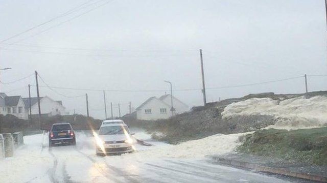 Sea foam blows into the road at Holyhead, cars on the road