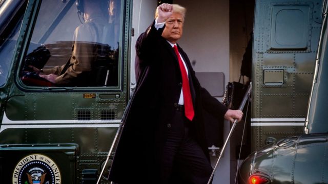 Donald Trump deixa a casa branca; de terno e com um punho levantado, sobe em um helicóptero verde escuro