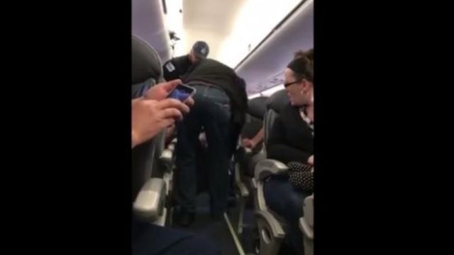 यात्री को विमान से बाहर निकालते सुरक्षाकर्मी