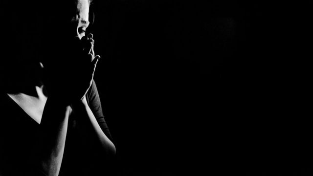 Mujer que se toma la cara con las manos en medio de sombras.