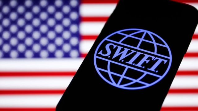 El logotipo de SWIFT se muestra en la pantalla del teléfono y la bandera estadounidense se muestra en el fondo