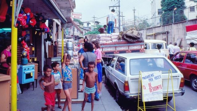 Crianças posam para foto próximas a uma área comercial no Jacarezinho. Carros passam ao lado