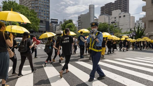 日本东京街头一名警员为通过马路的声援香港示威者维持秩序（12/6/2022）