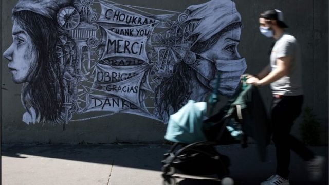 Homem caminha de máscara e com carrinho de bebê diante de mural na França