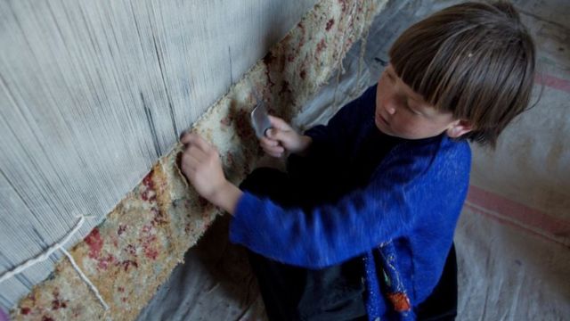 An eight-year-old child weaving a carpet