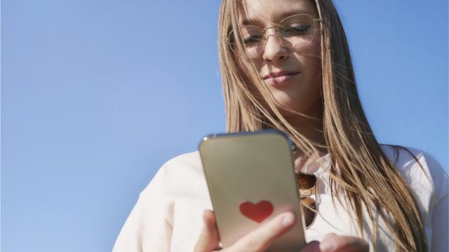 Mujer mira su teléfono, que tiene un sticker de corazón detrás.