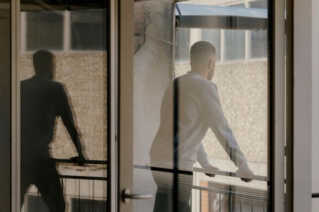 Fotografia mostra um homem de costas através de uma porta, olhando para fora em uma sacada
