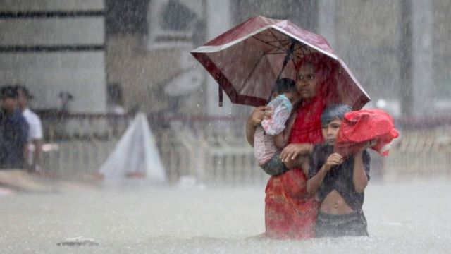 Bangladeş'in kuzeydoğusundaki Sylhet kentinde sele neden olan şiddetli yağmurların ortasında sığınacak yer arayan insanlar suda yürüyor, 18 Haziran 2022.