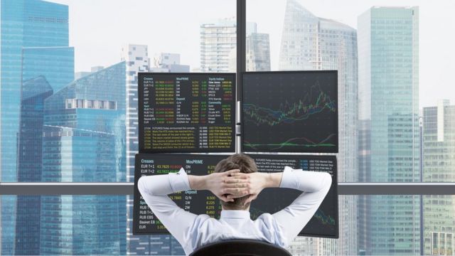 Inversor mirando sus acciones desde su oficina en un rascacielos