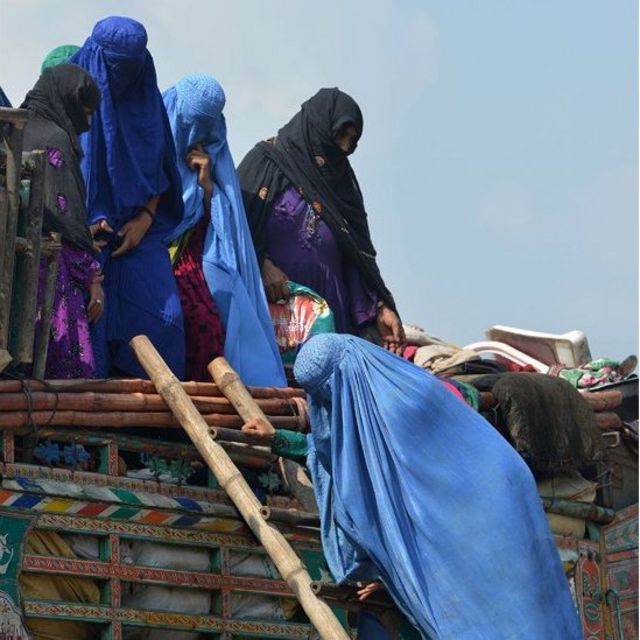 Mujeres afganas cubiertas con burkas intentan subir a un camión