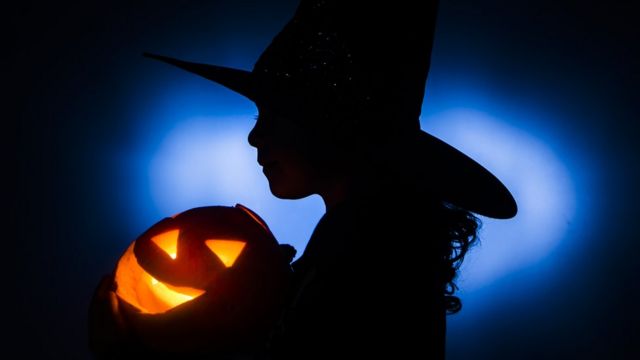 Silueta de una niña disfrazada de bruja con una calabaza de Halloween