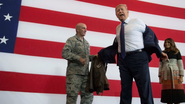 US President Donald Trump (C) takes off his suit jacket to receive a bomber jacket from the US Pacific Air Forces as First Lady Melania Trump (R) looks on during an event to speak to US military personnel at Yokota Air Base at Fussa in Tokyo, 5 November