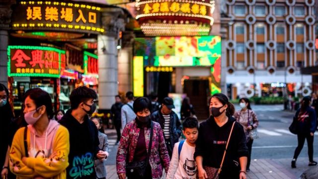 Imagen de personas caminando por una calle de Macao con carteles luminosos de fondo.