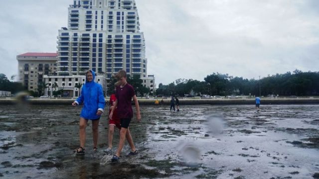 niños caminan por la arena una vez retrocedió el mar por el huracán Ian