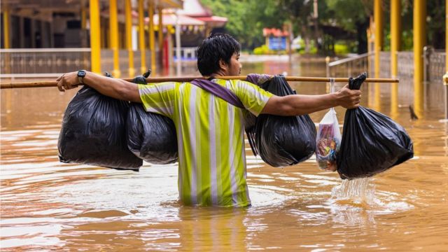 थाईल्यान्डमा भारी बोकेर जलमग्न सडक पार गर्दै एक मानिस