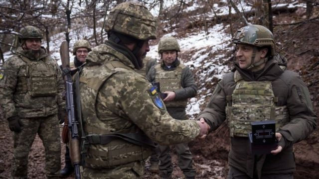 Presidente Volodymyr Zelensky aperta mão de militar, com outros observando ao fundo, em meio à neve