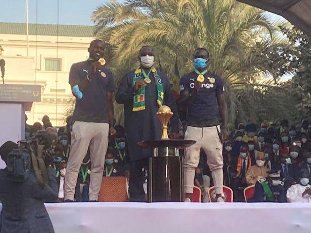 Le président Macky Sall debout entre Kalidou Koulibaly et Sadio Mané, médailles au cou