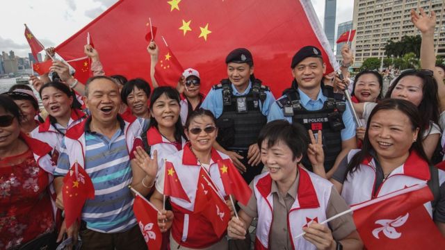 香港尖沙咀海旁手持中国国旗与香港特区区旗的亲北京政府群众簇拥着两名身穿防刺背心的警员合照（1/7/2023）