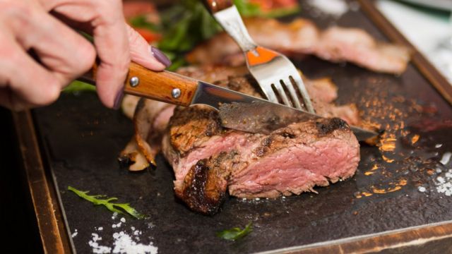 Imagem mostra mulher cortando pedaço de carne com garfo e faca. Algumas dietas com consumo reduzido de carboidratos são ricas nesse tipo de proteína animal, mas pesquisadores sugerem que elas sejam trocadas por proteínas vegetais, mais saudáveis