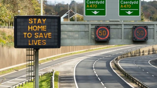 Carretera vacía rumbo a Cardiff en Gales con un cartel que dice "Quédate en casa, salva vidas"