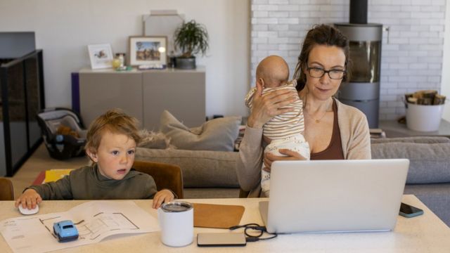 Mujer trabajando con sus hijos al lado.