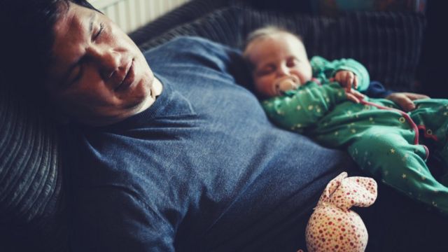 Padre dormido en el sofá con su hijo en brazos.