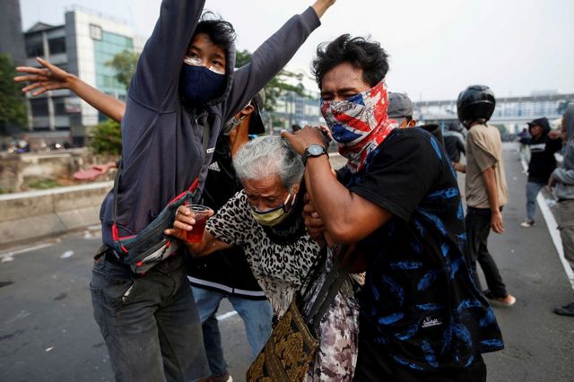 متظاهران في جاكارتا يحميان امرأة مسنة خلال اصطدامات في المدينة.