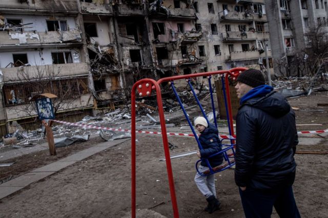 A boy plays on a swing in front of a damaged residential block in Kyiv hit by an early morning missile strike