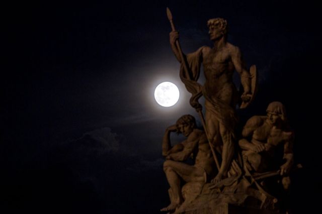 The pink supermoon rises through the clouds behind a statue of the Vittoriano in Rome, Italy