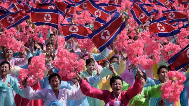 Participants wave flowers as they march past a balcony from where North Korea's leader Kim Jong Un was watching