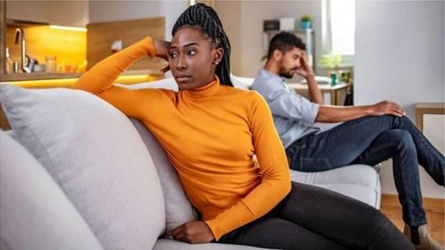 casal sentado de home e mulher negros, sentados em um sofá, cada um olhando para um lado