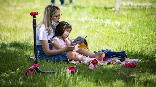 Menina lendo no colo da mãe em um parque