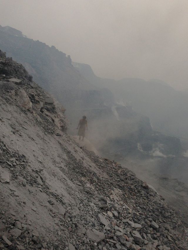 Un hombre camina sobre una montaña de carbón y ceniza.