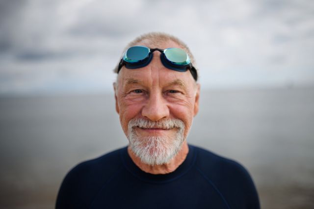 A smiling old man with swimming goggles on his head