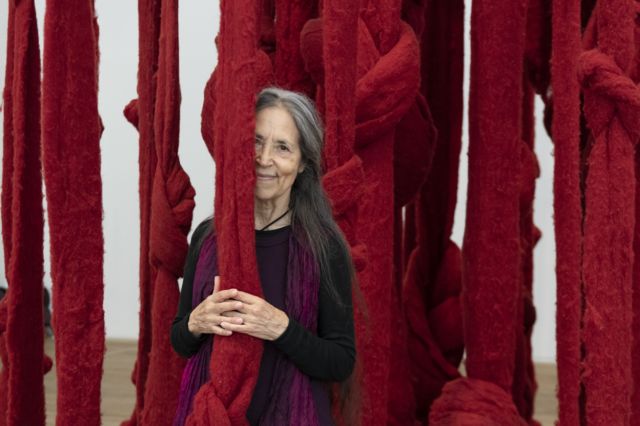 Cecilia Vicuña posa con su instalación Quipu Womb (2017). Foto de Lucy Dawkins