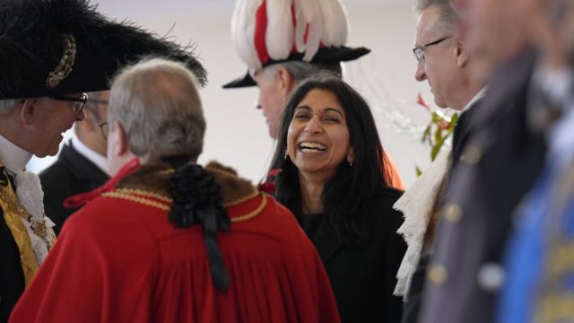 UK Home Secretary Suella Braverman laughs. She is surrounded by officials.