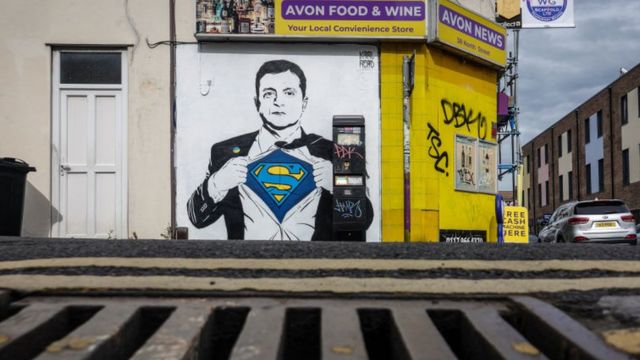 عمل فني للرئيس الأوكراني فولوديمير زيلينسكي يصوره كأنه سوبرمان على جدار أحد المتاجر، في 15 مايو/ أيار 2022 في بريستول، إنجلترا.