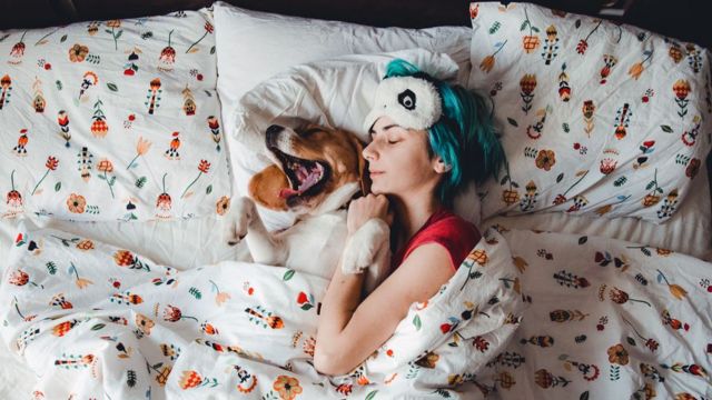Mulher dormindo com cachorro na cama