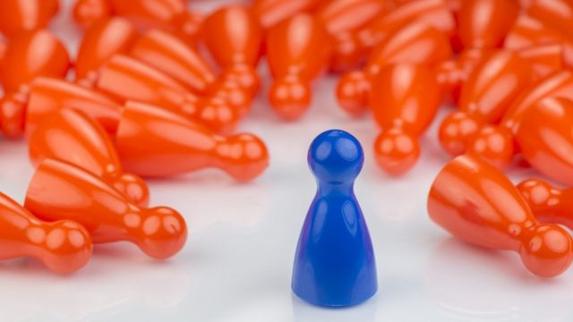 Un peón de ajedrez azul rodeado de peones naranjas.
