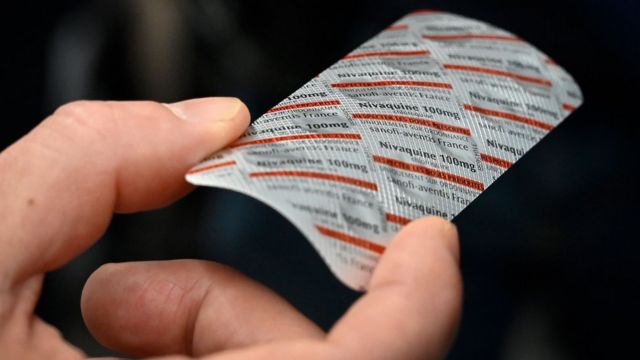 Uma mão segurando um pacote de Nivaquina, comprimidos contendo cloroquina