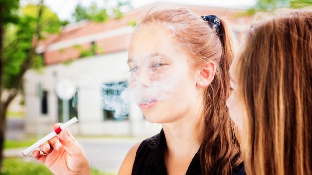 Dos preadolescentes fuman un cigarrillo electrónico.