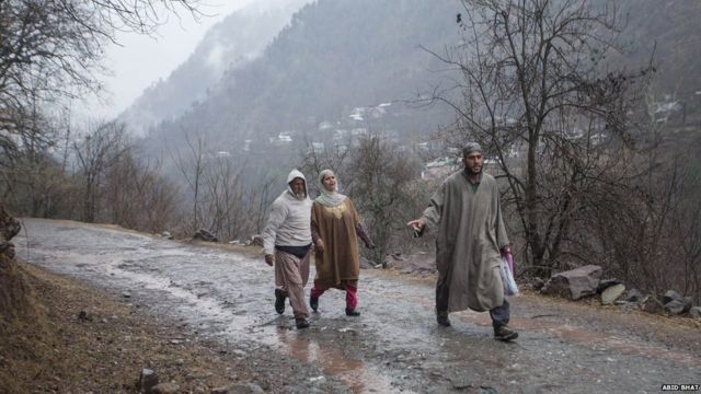 A Kashmiri family walks towards a vehicle as they leave home